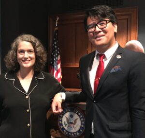 Jenny Collier with Trelaine Ito in US Senate Hearing Room. They are standing by a podium. The US Senate Seal is clearly visible.
